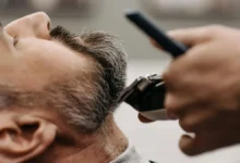 حلاق يقص شعر رجل يظهر عليه الشيب (الشعر الأبيض) في صالون حلاقة، للتركيز على علاج الشعر الابيض والاهتمام به.