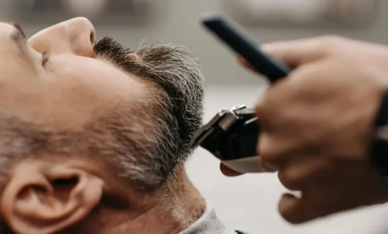 حلاق يقص شعر رجل يظهر عليه الشيب (الشعر الأبيض) في صالون حلاقة، للتركيز على علاج الشعر الابيض والاهتمام به.