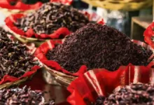 أوراق الكركديه المجففة باللون الأحمر الداكن معروضة في أوعية تقليدية بسوق شعبي.