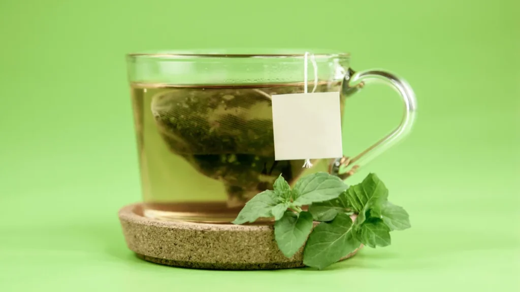 كوب شاي أخضر ساخن مع النعناع كيس شاي على قاعدة فلينية خلفية خضراء